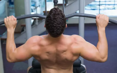 Hombre entrenando espalda con polea agarre cerrado. Músculos definidos trabajando en el gimnasio.