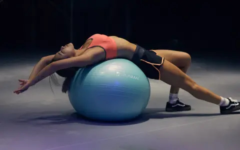 Mujer haciendo un curl femoral en fitball, estirando su espalda y brazos.