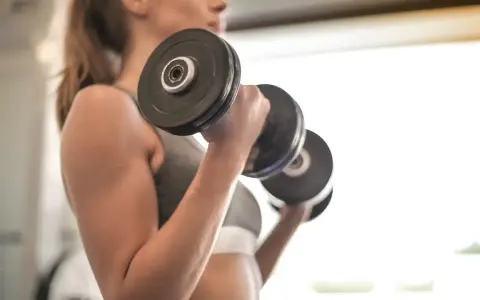 Mujer realizando ejercicio bíceps con mancuernas, enfocada en su entrenamiento.