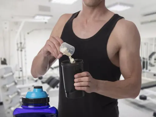 Hombre en gimnasio preparando batido con creatina para aumentar masa muscular.
