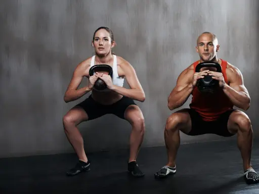 Hombre y mujer realizan sentadilla isométrica con kettlebell.