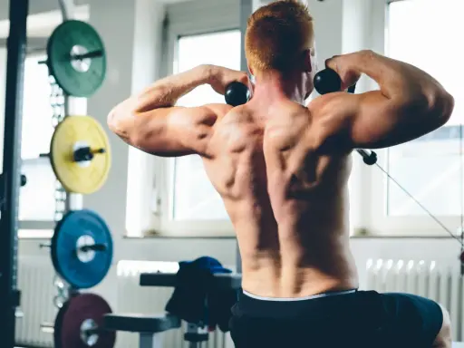 Hombre con espalda musculosa realizando un ejercicio de face pull sentado en el gimnasio.