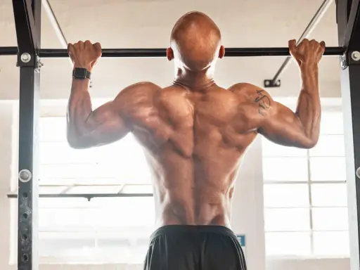 Hombre calvo haciendo dominadas, mostrando su espalda musculosa. Parte de su rutina de espalda gym.