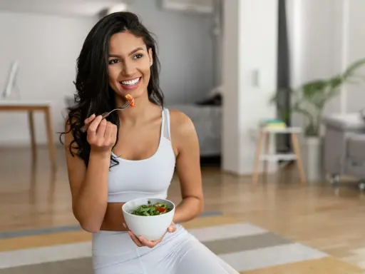 Mujer sonriente comiendo ensalada, equilibrando grelina y leptina para una vida saludable.