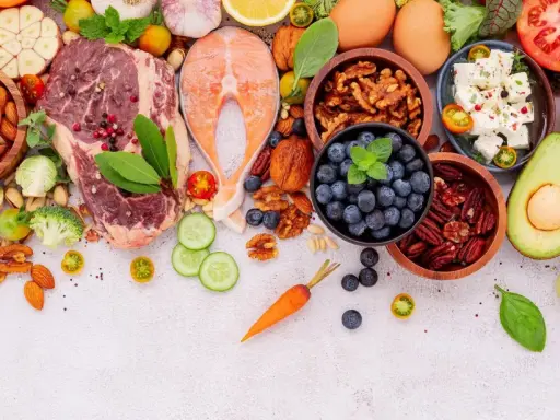 Ingredientes para un menú dieta keto: carne, salmón, huevos, aguacate, frutos secos, bayas, queso feta, verduras y hierbas frescas.