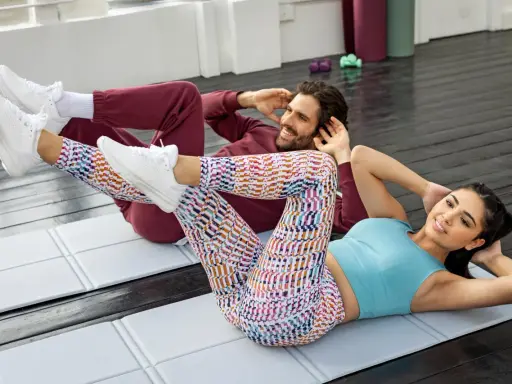 Pareja haciendo plancha con elevación de pierna en colchonetas.
