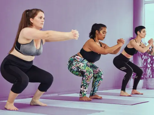 Tres mujeres realizan sentadilla con apoyo en un estudio de yoga.