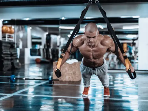 Hombre musculoso realizando trx ejercicios en un gimnasio, con el cuerpo tenso y sudoroso.