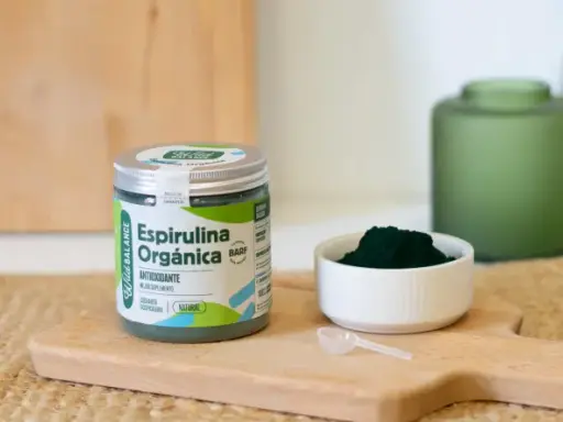 Un frasco de espirulina orgánica y una cucharita dosificadora sobre una tabla de madera. La espirulina es un superalimento antioxidante.
