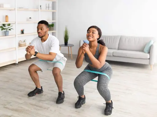 Pareja haciendo sentadillas con bandas elásticas para glúteos en casa.