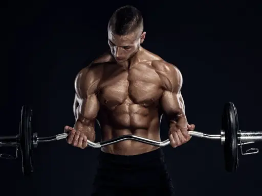 Hombre musculoso realizando curl en banco Scott con barra Z.
