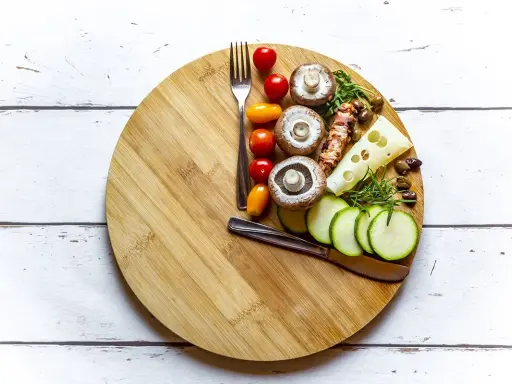Tabla de cortar con ingredientes saludables: champiñones, tomates, calabacín, queso y aceitunas. Ideas para saber qué comer para romper el ayuno intermitente 16/8.