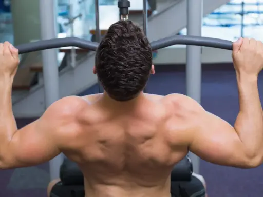 Hombre entrenando espalda con polea agarre cerrado. Músculos definidos trabajando en el gimnasio.