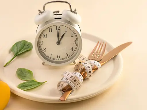 Reloj, plato, cubiertos con cinta métrica y hojas verdes. Símbolos de los beneficios del ayuno intermitente y un estilo de vida saludable.