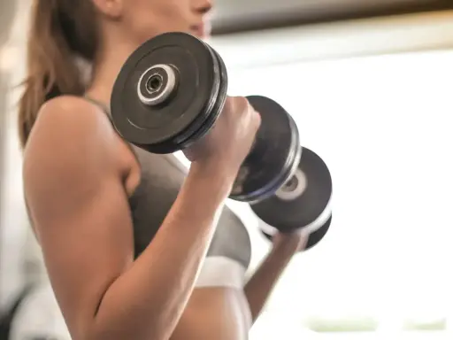 Mujer realizando ejercicio bíceps con mancuernas, enfocada en su entrenamiento.