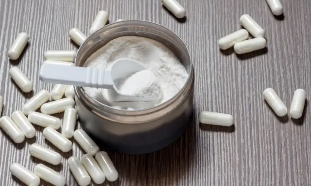 Cápsulas y polvo blanco sobre fondo de madera. Descubre para qué sirve la L-arginina y sus beneficios.
