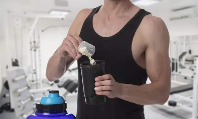 Hombre en gimnasio preparando batido con creatina para aumentar masa muscular.