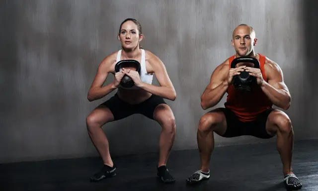 Hombre y mujer realizan sentadilla isométrica con kettlebell.