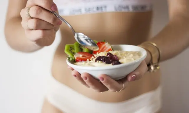 Mujer disfrutando un tazón de avena con fresas, kiwi y frutos secos. Un desayuno ideal para una dieta deficit calorico.