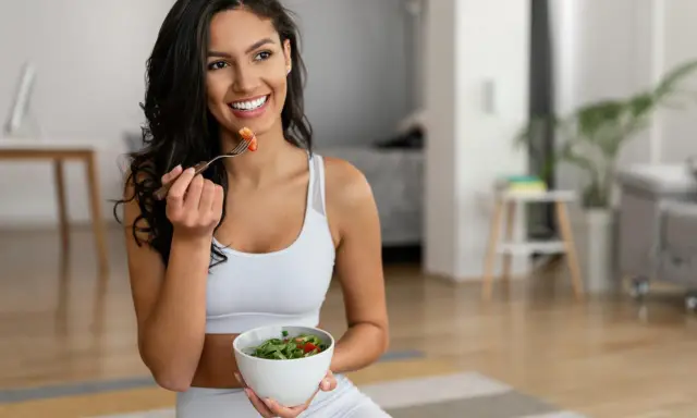 Mujer sonriente comiendo ensalada, equilibrando grelina y leptina para una vida saludable.
