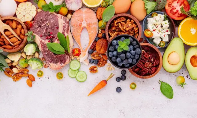 Ingredientes para un menú dieta keto: carne, salmón, huevos, aguacate, frutos secos, bayas, queso feta, verduras y hierbas frescas.