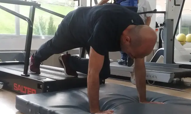 Hombre realizando ejercicio de cuadrupedia en una cinta de correr, con manos apoyadas en colchoneta.