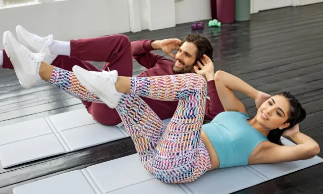 Pareja haciendo plancha con elevación de pierna en colchonetas.