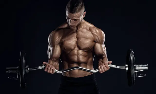 Hombre musculoso realizando curl en banco Scott con barra Z.