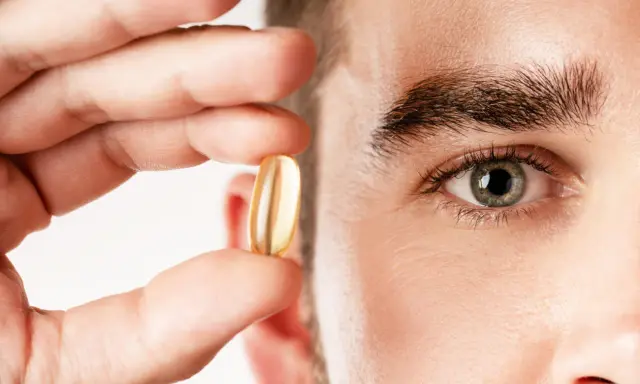 Un hombre sostiene una cápsula de aceite de pescado, destacando los omega 3 beneficios para hombres.