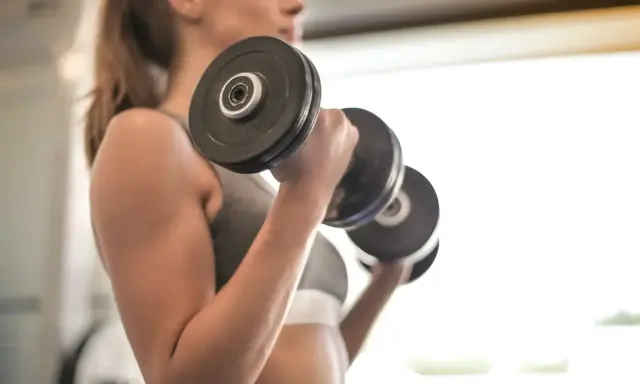 Mujer realizando ejercicio bíceps con mancuernas, enfocada en su entrenamiento.