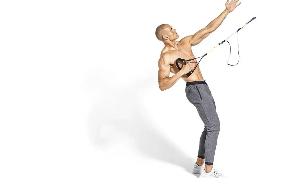 Hombre musculoso realiza ejercicio de remo TRX, con su brazo extendido hacia arriba y el otro sujetando las asas.