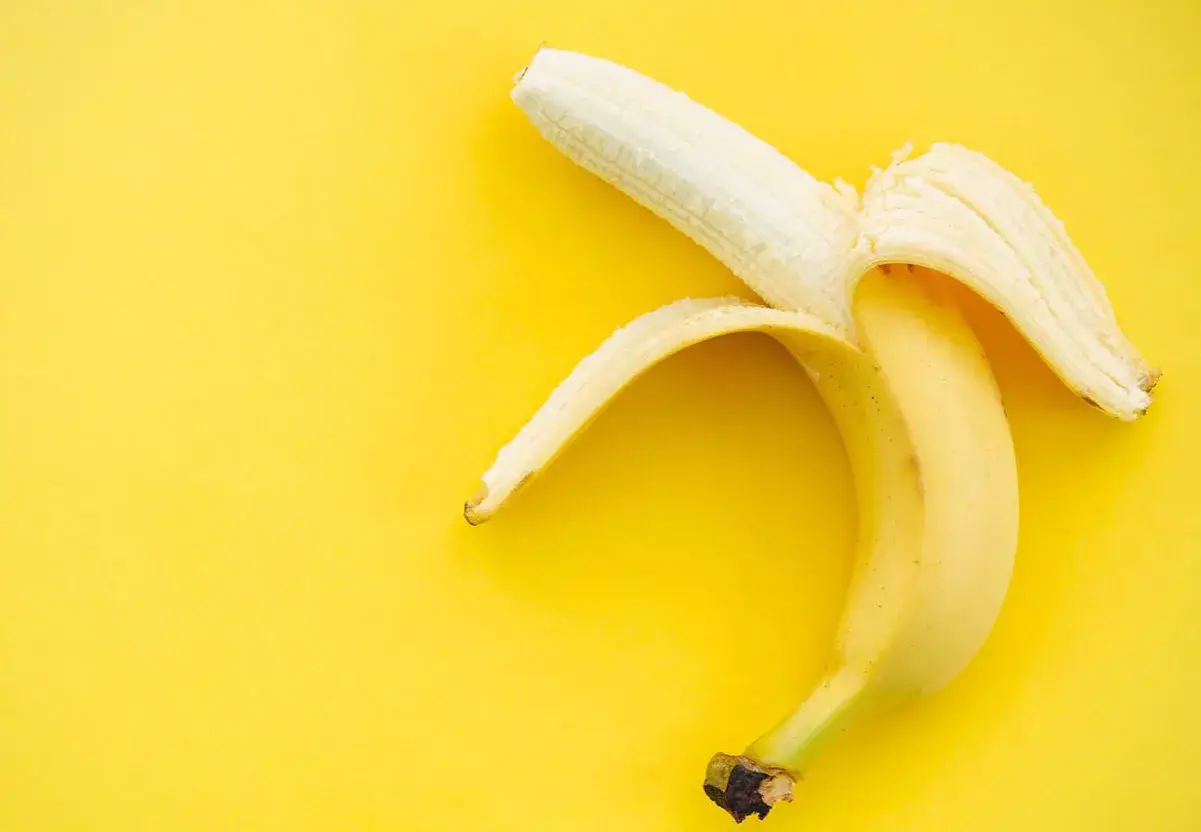 Plátano pelado sobre fondo amarillo. Un snack saludable con pocas calorías, ideal para deportistas.