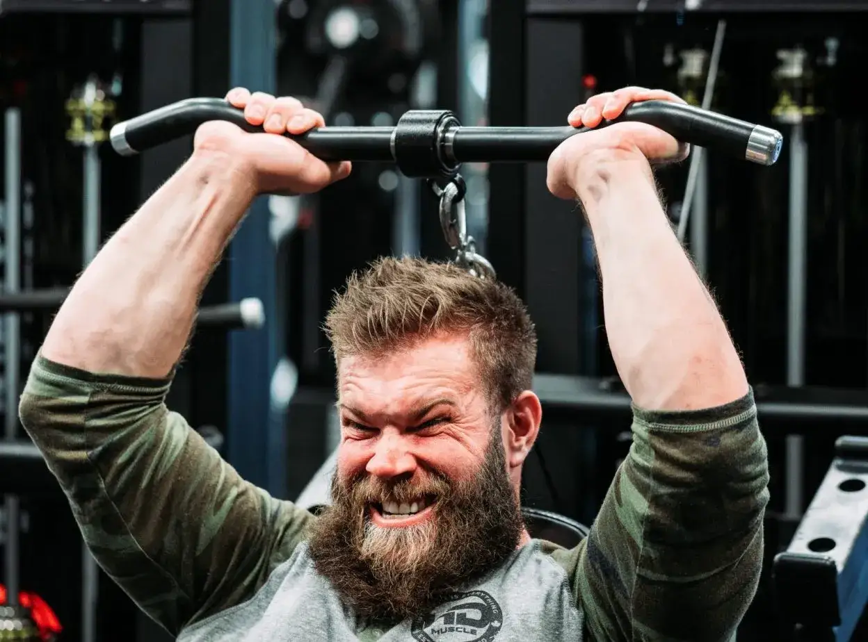 Hombre con barba haciendo extensi&oacute;n de triceps en m&aacute;quina, concentrado y con esfuerzo.