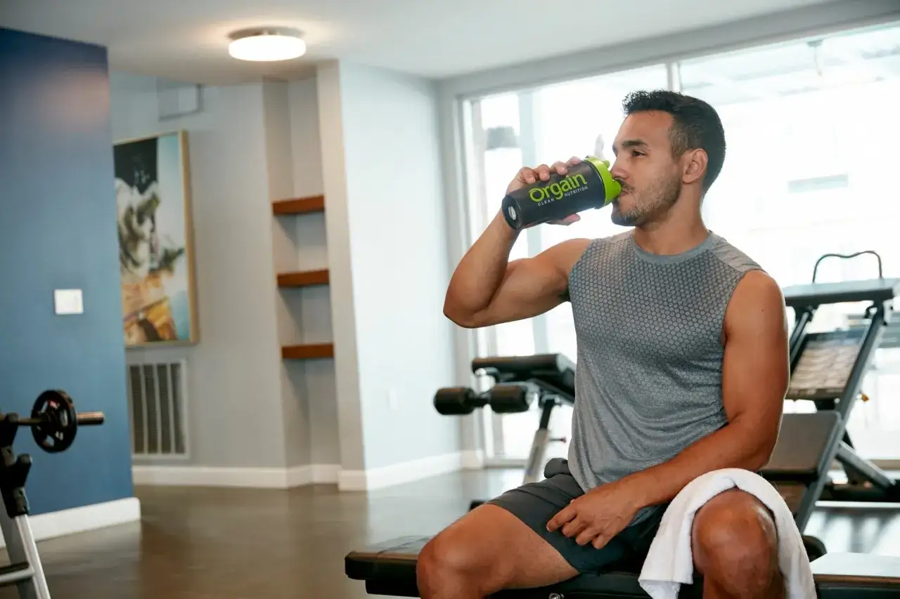 Hombre en el gimnasio bebe prote&iacute;na de Orgain. Un momento ideal para saber cuando tomar prote&iacute;nas y optimizar tu entrenamiento.