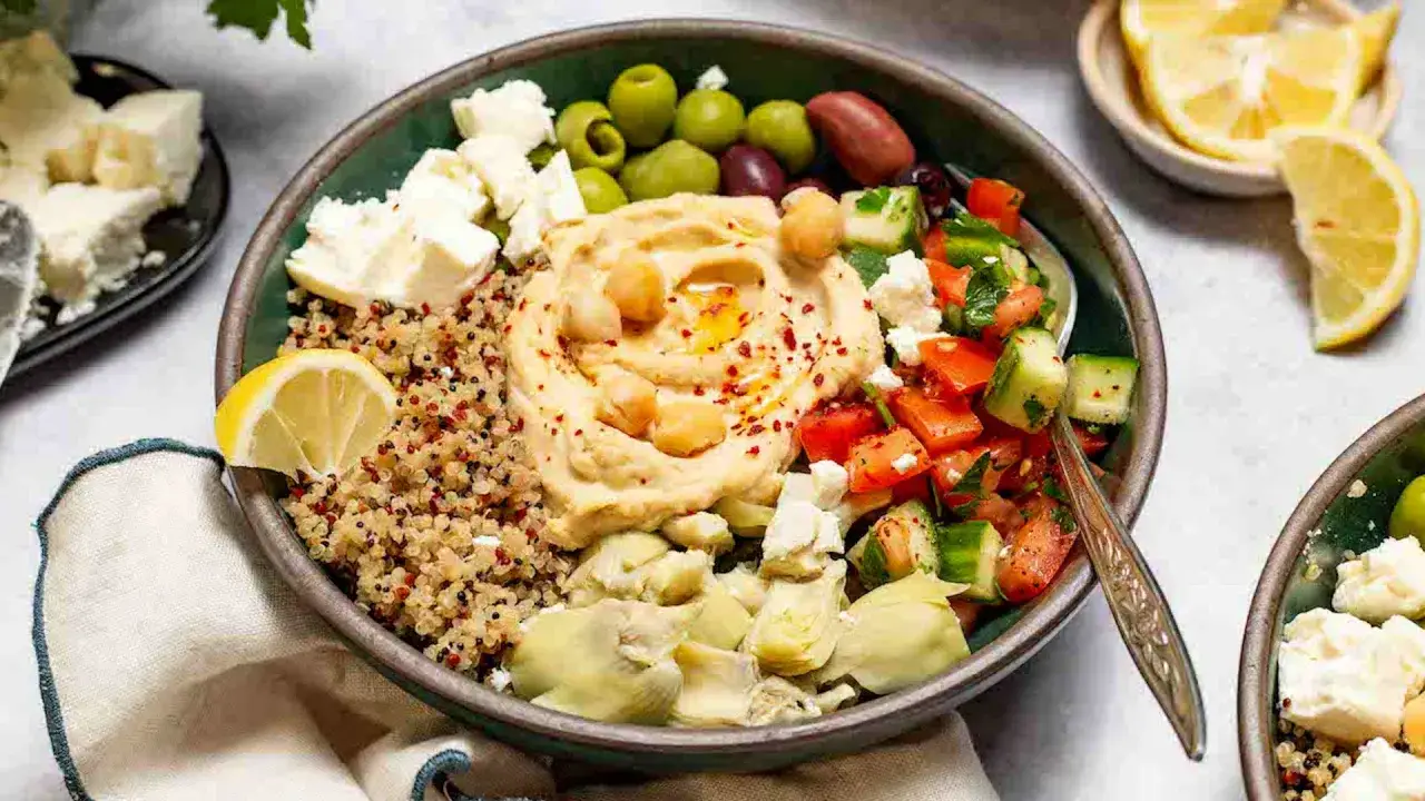 Bowl con quinoa, hummus, verduras, aceitunas y queso feta. Ideal para una dieta para osteoporosis, rica en calcio y nutrientes.