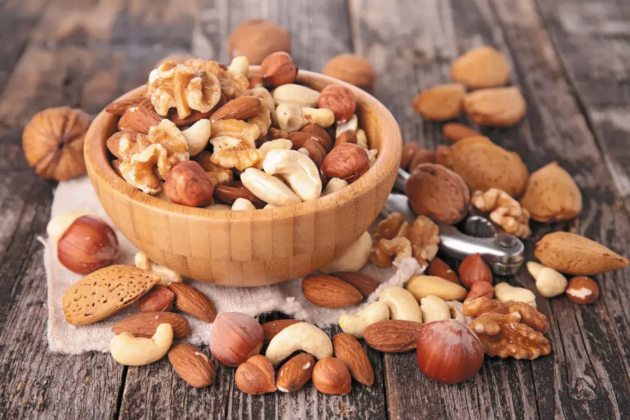 Un cuenco de madera rebosa de frutos secos variados: nueces, almendras, anacardos y avellanas. Alrededor, m&aacute;s frutos secos y un cascanueces, record&aacute;ndonos que los frutos secos engordan si no se consumen con moderaci&oacute;n.