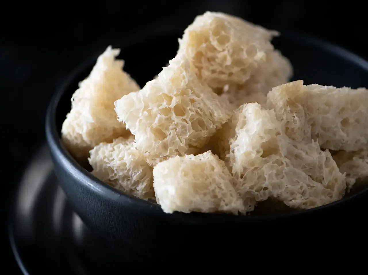 Trozos de seitan que es, con su textura esponjosa y alveolada, servidos en un cuenco oscuro.
