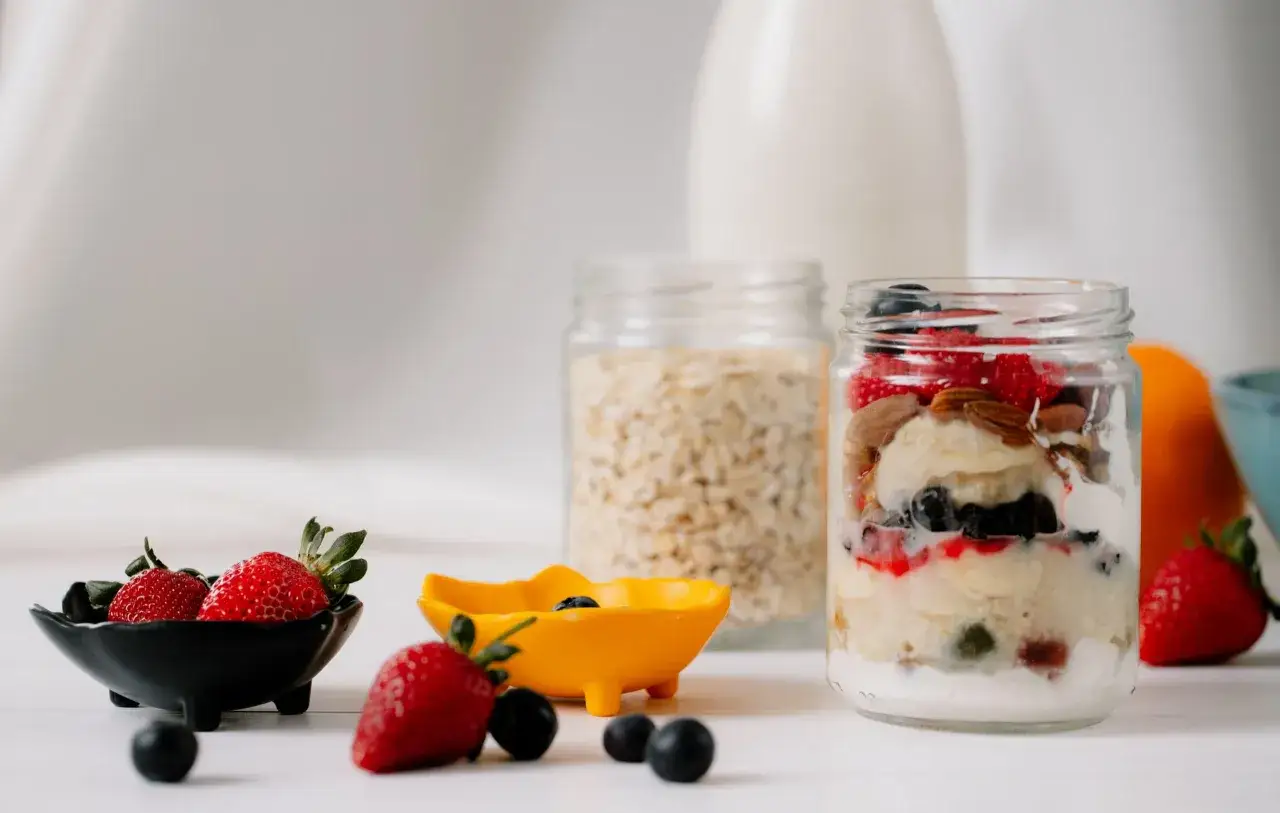 Un delicioso snack en capas: yogur, avena, fresas, ar&aacute;ndanos y almendras en un frasco.