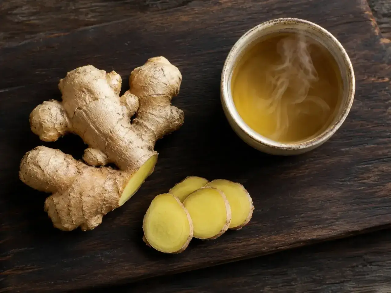 Raíz de jengibre fresca y rodajas junto a una taza de té humeante, mostrando los beneficios del jengibre para la salud.