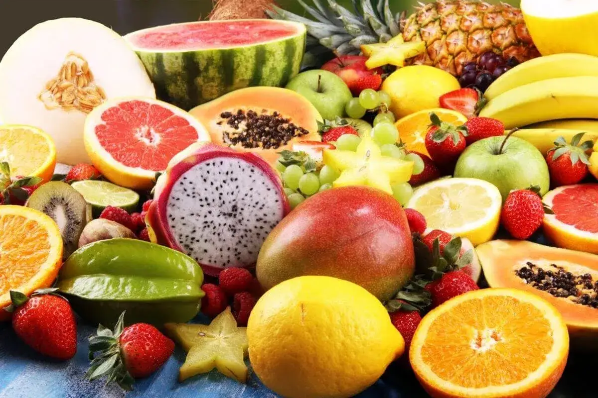 Un surtido vibrante de frutas frescas, incluyendo mangos, fresas, naranjas y uvas, todas ricas en fructosa natural.