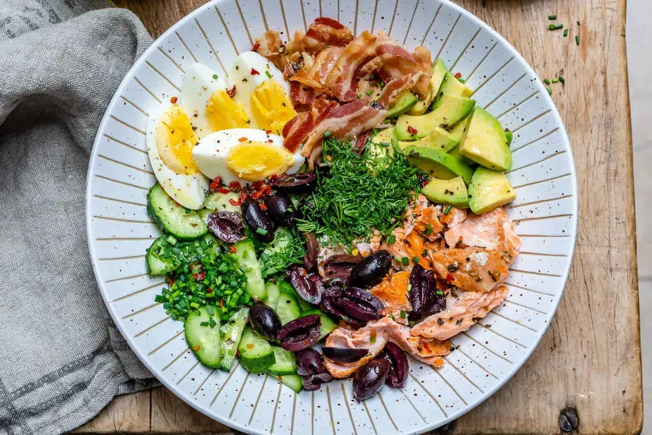 Plato con salmón, huevos duros, aguacate, pepino, aceitunas y tocino. Un festín de alimentos bajos en carbohidratos.