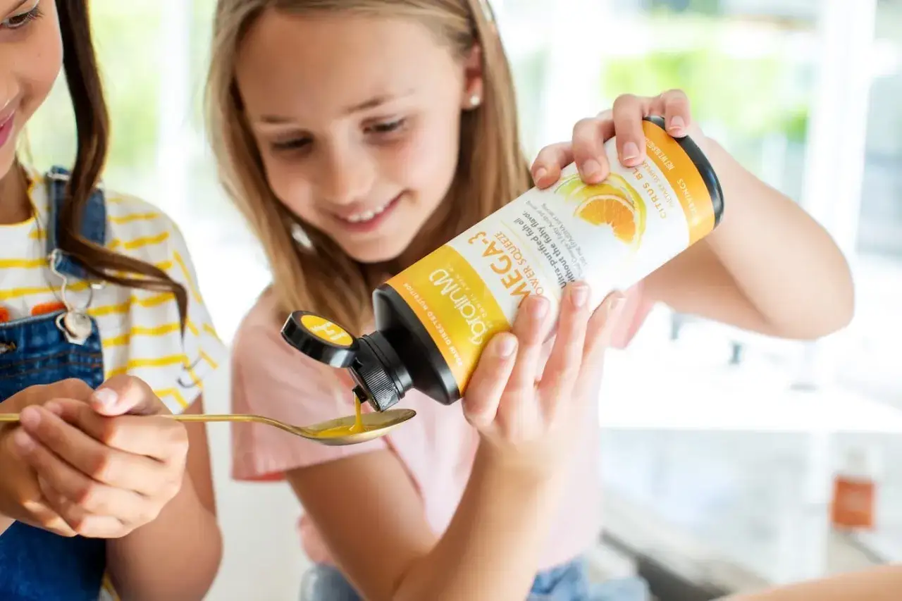 Niña sonriente vierte omega 3 para niños con TDAH en una cuchara.