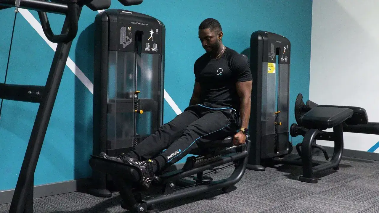 Hombre entrenando gemelos sentado en m&aacute;quina de gimnasio.