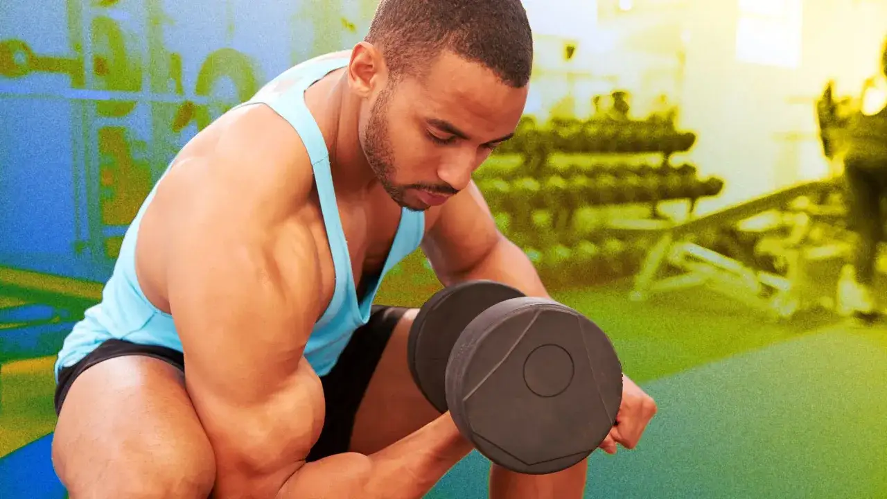 Hombre concentrado realizando ejercicio b&iacute;ceps con mancuerna en el gimnasio.
