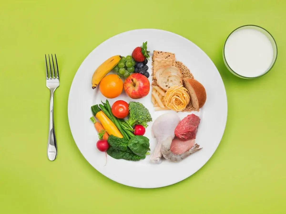 Plato con variedad de alimentos bajos en calorías: frutas, verduras, granos, proteínas y un vaso de leche.