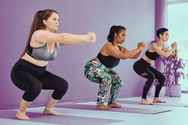 Tres mujeres realizan sentadilla con apoyo en un estudio de yoga.