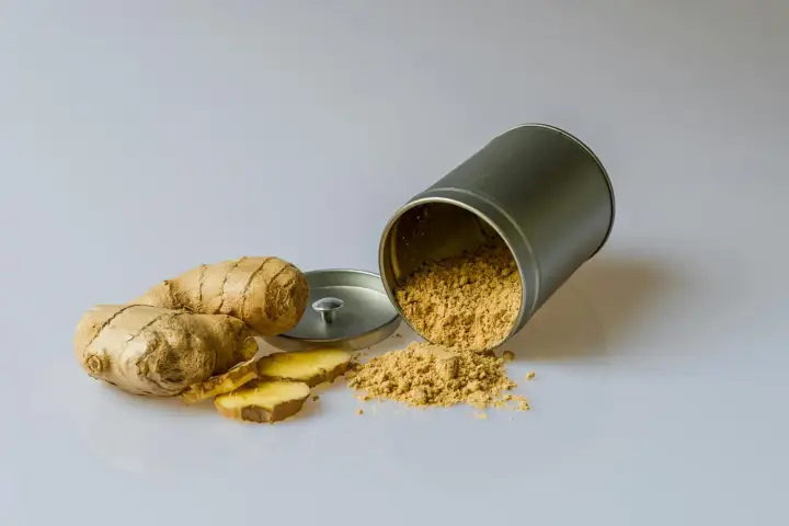 Raíces de jengibre y polvo esparcido de un recipiente, mostrando los **beneficios del jengibre** para la salud.